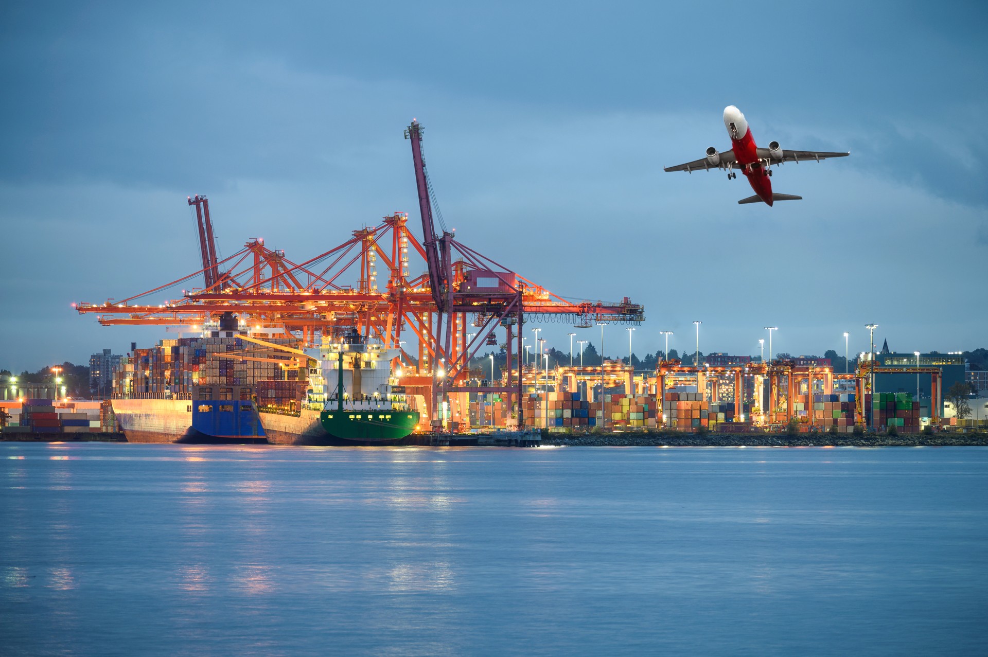 Airplane flying over a container port and cargo ships