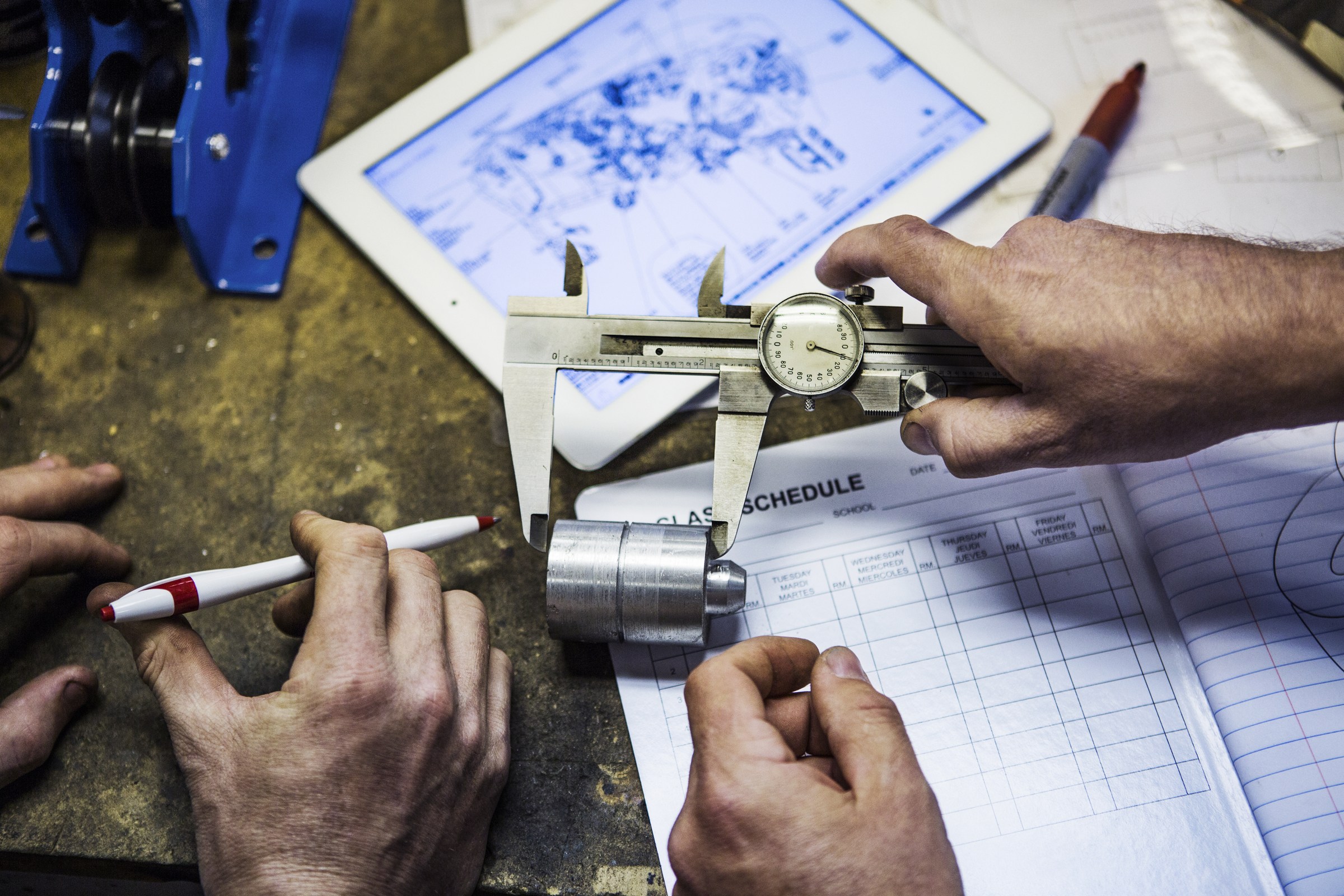 Metal component checked with a caliper alongside technical drawings and inspection records